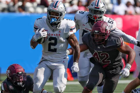 Football players wearing Morehouse and Howard jerseys playing football on a field in front of a crowd.
