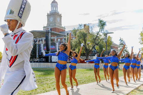 Drum major in band uniform and majorettes marching through the Yard on a sunny day.