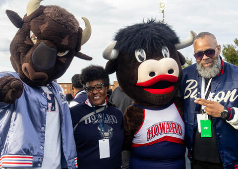 Two Howard mascots standing with alums posing and smiling at a Homecoming game outside